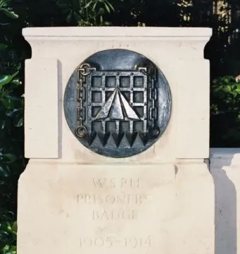 W.S.P.U. prisoners\' badge plaque on the Pankhurst Memorial stone plinth, with foliage in the background.