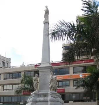 The Triumph of the Candelaria obelisk rises in an open plaza, with stone figures at the base and a white figure atop the monument.
