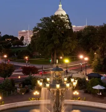 Bartholdi Fountain lit at dusk with water spraying into a circular basin, with the illuminated Capitol dome in the background.