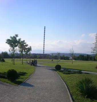 The Endless Column rises above a green park with trees, paths, and distant mountains.