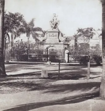 Fuente de la India stone fountain with a seated woman statue, carved sea creatures, and a surrounding iron fence.