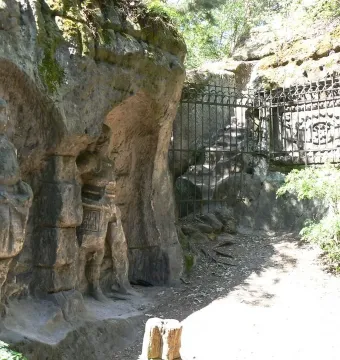 Two carved knight figures in the Klácelka rock face beside a metal gate and railings.