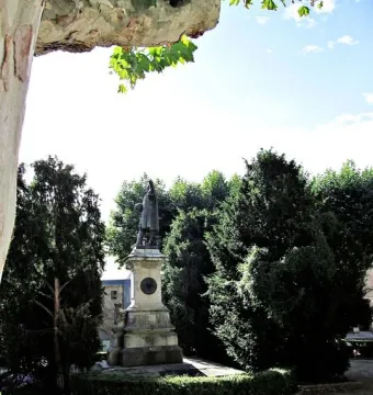 Monument to Columbus on a tall stone pedestal surrounded by trees and a circular hedge.