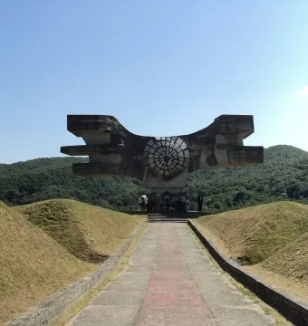 The Monument to the Revolution of the People of Moslavina, a large angular concrete sculpture with a circular center, standing among green hills.