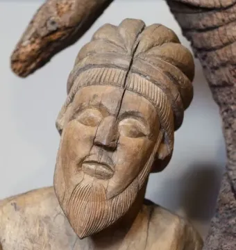 Close-up of a carved wooden head from the Descent from the Cross, showing a textured turban and pointed beard with a vertical split in the face.