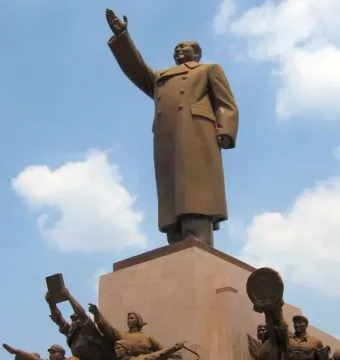 Bronze monument of Mao Zedong with his right arm raised, surrounded by smaller figures at the base.