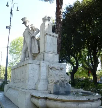 Monument to Giuseppe Gioachino Belli with a statue of a man in a top hat and long coat, beside a fountain with a grotesque face and round basin.