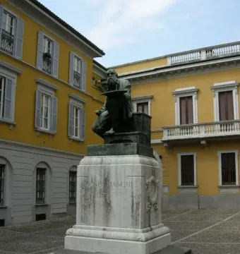 Bronze monument to Mose Bianchi showing a seated bearded man holding a painter\'s palette on a stone pedestal.