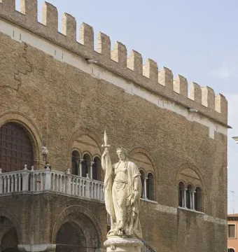 Monumento dell\'Indipendenza statue of a draped female figure holding a spear in front of a historic brick building.