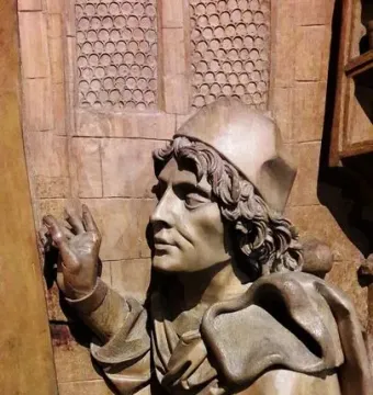 Wooden sculpture of Saint Luke in profile with raised hands and draped robes.