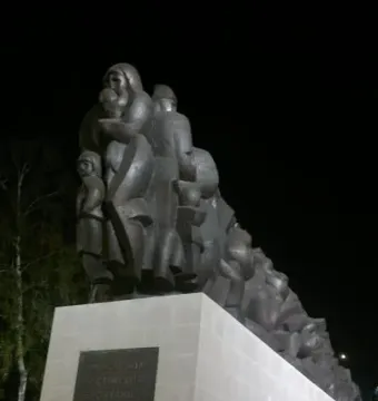 The Train of Pain monument showing a dark sculptural relief of families and children on a stone base at night.