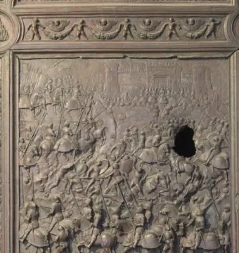 Bronze Gate bronze relief panel showing a chaotic battle scene with horsemen and foot soldiers, damaged by a large hole on the right side.
