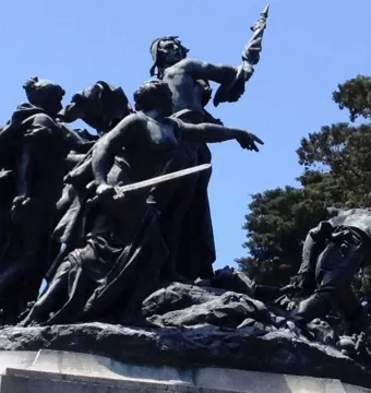 Bronze figures on the National Monument of Costa Rica against a blue sky, with one figure holding a sword and another pointing.