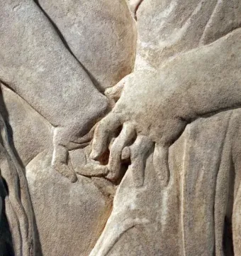 Detail of the Pulpit of Prato Cathedral showing carved hands amid draped folds in stone relief.