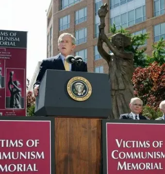 Victims of Communism Memorial statue of a draped female figure holding a torch overhead, with red signs in the foreground.