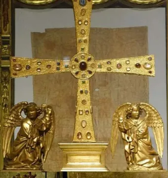 The Cross of the Angels displayed with winged angel statues and a gilded reliquary casket beside it.