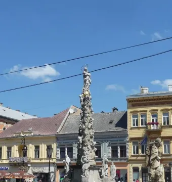 Marian Column with a haloed statue of the Virgin Mary, surrounded by figures and a metal fence.