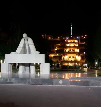 Monument to Alexander Tamanyan at night with the illuminated Cascade complex in the background.