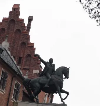 Tadeusz Kościuszko Monument, a dark equestrian statue of a man in a long coat with one arm raised, against a bright overcast sky.