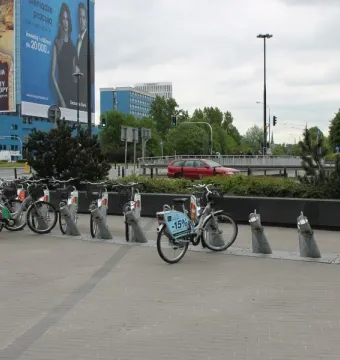 Bicycle rental station with docked bikes on a paved city square.