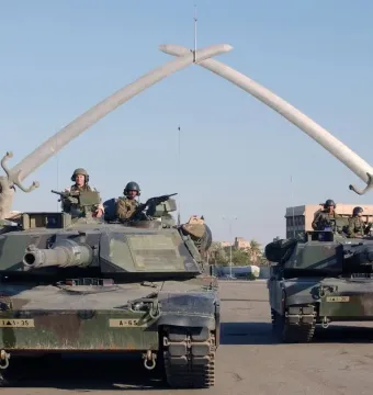 Victory Arch in Baghdad, with two tanks positioned beneath the crossed swords monument held by giant sculpted hands.