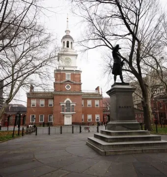 Commodore John Barry statue on a stepped stone pedestal in front of a historic brick building with a clock tower.