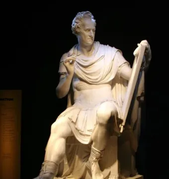 Seated George Washington sculpture in white stone, holding a stylus and tablet, with an information panel beside it.