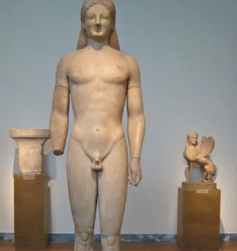 Kouros marble statue of a nude male figure with a missing left forearm and long braided hair.