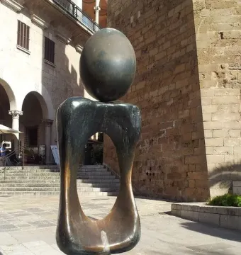 Monument a la dona bronze sculpture with a dark oval sphere balanced on an abstract hollow form outdoors.