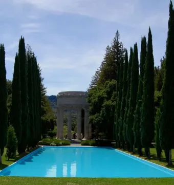 Pulgas Water Temple with a long blue reflecting pool, stone rotunda, and tall evergreen trees lining the avenue.