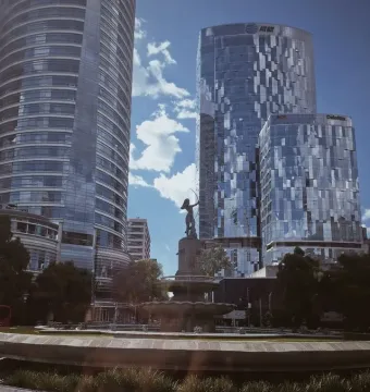 Diana the Huntress Fountain with a dark bow-wielding figure, framed by trees and modern skyscrapers.