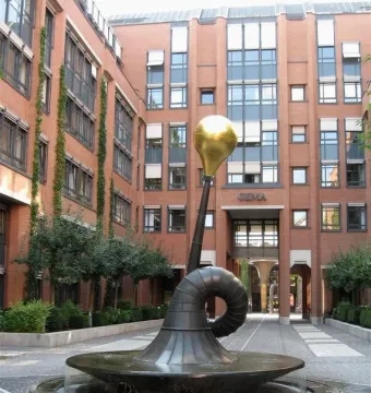 Erich-Schulze-Brunnen, a dark metal fountain with a curved trumpet-like form topped by a gold sphere in a paved courtyard.