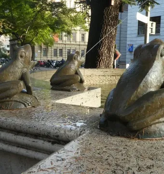 Three bronze frog sculptures on the Fountain of the Frogs spouting water from a stone basin.