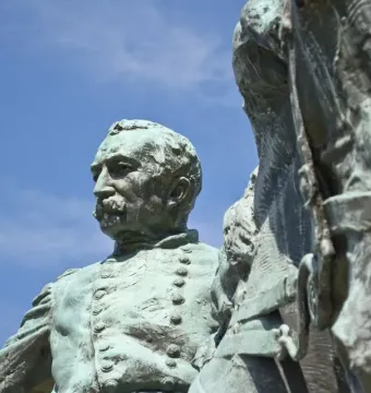 Close-up of the bronze General Philip Sheridan statue with a green patina against a blue sky.