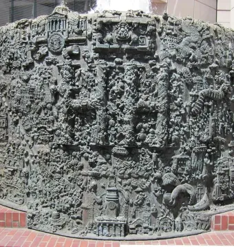 San Francisco Fountain with a highly textured metallic surface and intricate raised details in front of a red-brick platform.