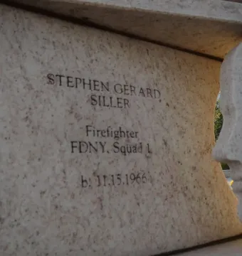 Stone monument engraved with Stephen Gerard Siller’s name and firefighter details beside a sculpted human face profile.