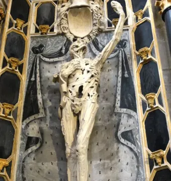 Transi of René of Chalon, an emaciated stone figure holding a heart to its chest in a dark niche.