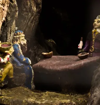 Carved figures inside the Elfin Oak, including a jester, a bearded king in blue, and colorful elf-like characters gathered around a table.