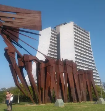 The Monument to the Azoreans, a tall reddish-brown metal sculpture on a grassy lawn with modern buildings behind it.