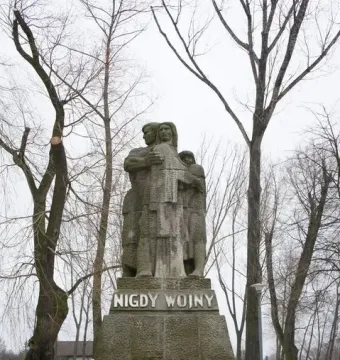 War Never Again stone monument showing a man embracing a woman and child on a tiered base inscribed “NIGDY WOJNY.”