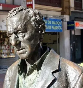 Woody Allen Memorial sculpture torso in dark metal, shown outdoors with storefronts blurred behind it.