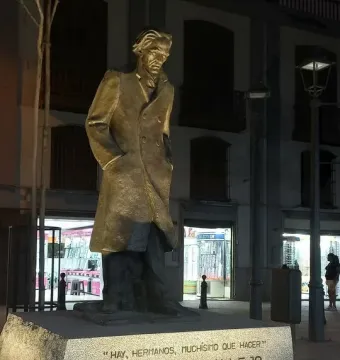 The Monument to César Vallejo stands on a stone base in a lit plaza at night.