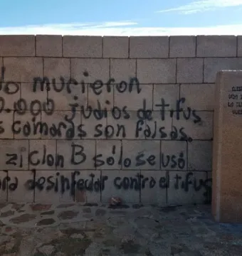 Graffiti-covered wall at the Holocaust Memorial in Uruguay beside a stone pillar with engraved text.