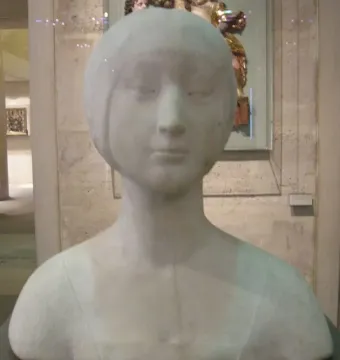 White marble bust of a princess with downcast eyes and a simple bob hairstyle, displayed in a museum gallery.