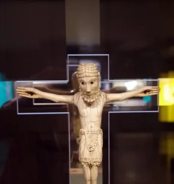 Carrizo Christ crucifix with outstretched arms, carved details, and a decorated loincloth displayed in a case.