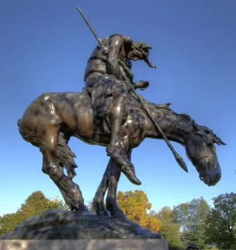End of the Trail bronze statue of a slumped rider on horseback holding a spear, with bowed heads against a blue sky.