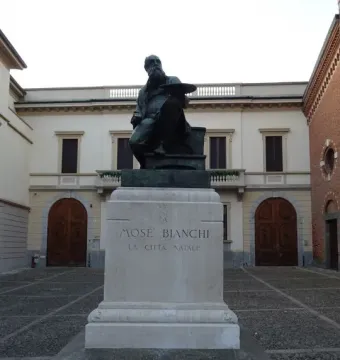 Monument to Mosè Bianchi showing a bronze seated statue of the bearded artist holding a palette on a stone pedestal.
