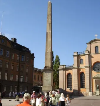 The Obelisk at Slottsbacken rises from a cobblestone plaza with people gathered around it.