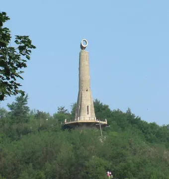 The Thanksgiving Candle monument rises from a wooded hill under a clear blue sky.
