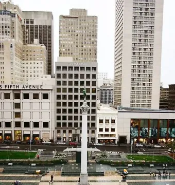 Dewey Monument rising from a large urban plaza with checkered pavement, surrounded by city buildings and streets.